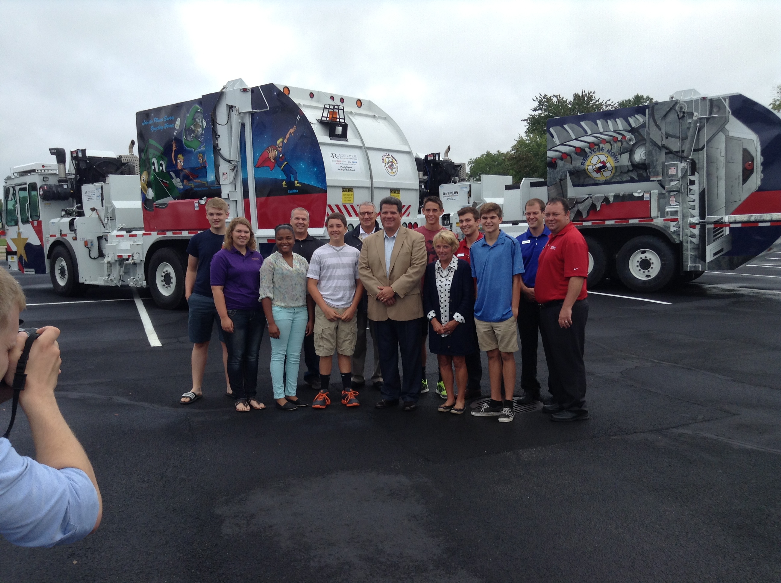 A group of people standing in front of brand new trash trucks